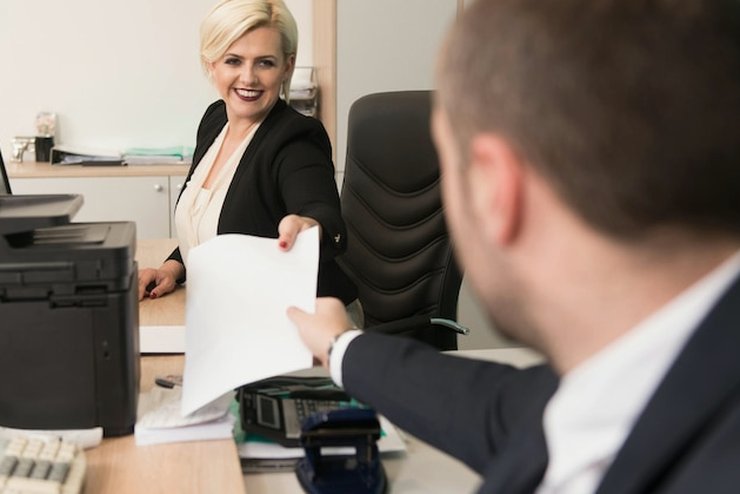 A document being handed over at a front desk beside an office printer