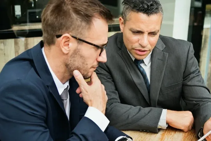 Two men in suits going over notes at a wooden table